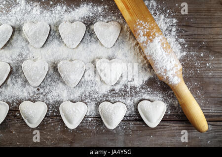 Herzförmige Ravioli mit Flou und Nudelholz auf Vintage Holztisch Hintergrund. Knödel kochen. Ansicht von oben. Stockfoto