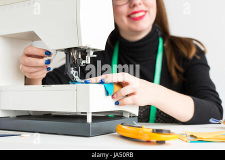 Nähen und Quilten in der Werkstatt von einer jungen Frau - Schneider mit einem hellen Maniküre arbeiten an einem Schreibtisch mit einer Nähmaschine-Nahaufnahme Stockfoto