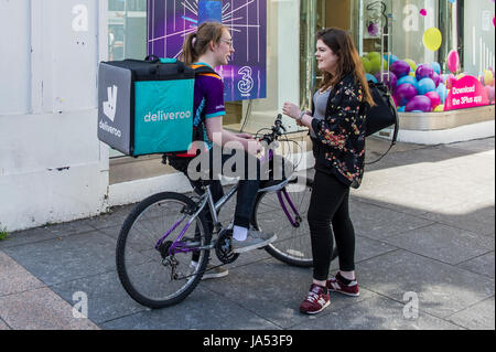 Deliveroo weibliche Lieferung Reiter im Gespräch mit einem Freund während einer Pause in Cork, Irland. Stockfoto