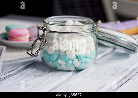 Marshmallows in weiß und blau Pastell auf einer hellen Holzoberfläche. In ein Glas mit einem aufklappbaren Deckel Stockfoto