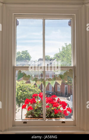 Innenraum eines viktorianischen britischen Hauses mit alten Holzfenster weißen und roten Geranien auf der Fensterbank mit Blick auf eine traditionelle englische Straße Stockfoto