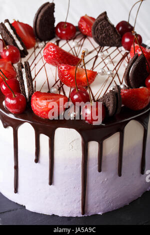 Schöner Kuchen mit Erdbeere und Kirsche, verzierte Plätzchen und Schokolade close-up auf dem Tisch. vertikale Stockfoto