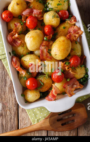 Leckere neue Kartoffeln gebacken mit Speck, Kräutern und Tomaten-Makro in eine Auflaufform legen. vertikale Ansicht von oben Stockfoto