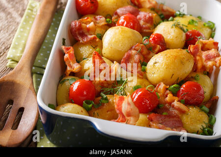 Leckeres Essen: frische Kartoffeln gebacken mit Speck, Frühlingszwiebeln und Tomaten Nahaufnahme in eine Auflaufform legen. horizontale Stockfoto