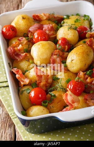 Naturkost: Gebackene Kartoffeln mit Speck, hautnah grüne Zwiebeln und Tomaten in die Auflaufform. vertikale Stockfoto