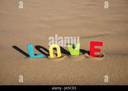 LIEBE geschrieben mit bunten hölzernen Buchstaben Text auf Sand einer Düne Stockfoto