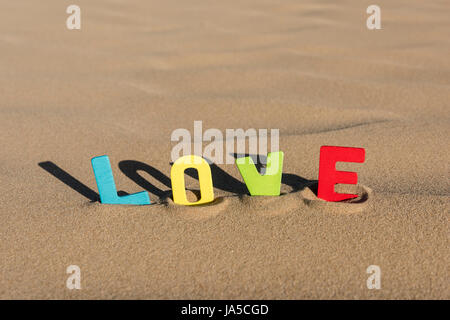 LIEBE geschrieben mit bunten hölzernen Buchstaben Text auf Sand einer Düne Stockfoto