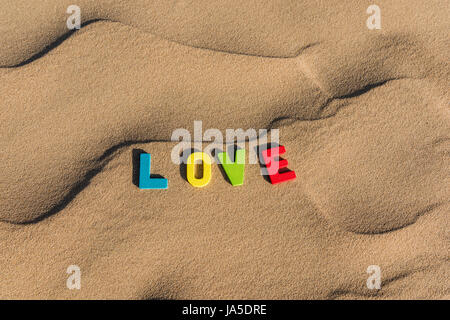 LIEBE geschrieben mit bunten hölzernen Buchstaben Text auf Sand einer Düne Stockfoto