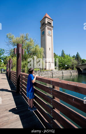 Ein kleiner Junge steht auf dem Geländer, Blick auf den Uhrturm im RIverfront Park in Spokane, Washington. Stockfoto