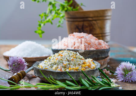 Verschiedene Arten von Natursalz in Stein Schalen auf der Holzoberfläche. Weißes Meer Salz, rosa Himalaya Salz, Salz gewürzt mit Rosmarin Stockfoto