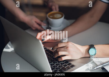 Draufsicht der Weibchen mit ihrem Laptop in einem Café. Overhead Schuss von junge Frau sitzt an einem Tisch mit einer Tasse Kaffee und Handy-Surfen im Netz auf ihrem Laptop-Computer. Stockfoto