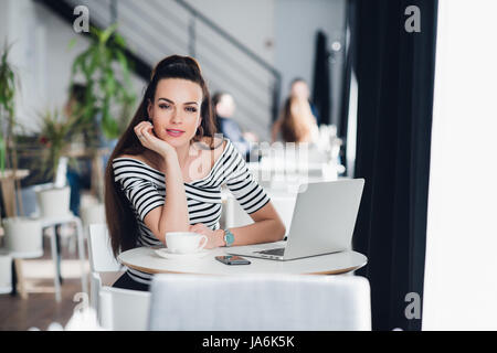 Porträt der jungen Frau mit Laptop und Handy in einem Straßencafé sitzen. Stockfoto