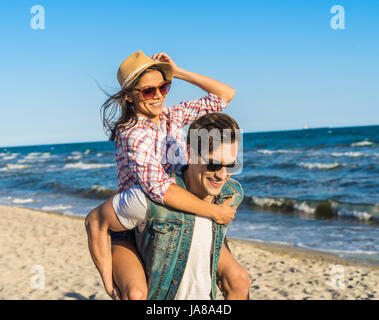 junge lustige paar Sonnenbrillen Huckepack auf den Strand. Stockfoto