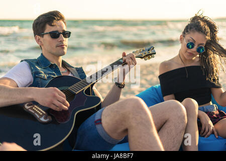 Gitarre-Spaß. Hübscher Junge Hipster Mann spielt Gitarre am Strand Stockfoto