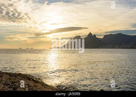 Arpoador Beach in Rio De Janeiro, mit seinen Steinen, Gebäuden und Meer bei Sonnenuntergang und die beiden Brüder Hill im Hintergrund Stockfoto