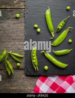 Offene und geschlossene Pellets von grünen Erbsen auf einem schwarzen Stein Hintergrund. Frisches Obst. Die Ernte. Ansicht von oben. Stockfoto