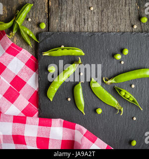 Offene und geschlossene Pellets von grünen Erbsen auf einem schwarzen Stein Hintergrund. Frisches Obst. Die Ernte. Ansicht von oben. Stockfoto