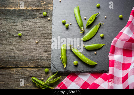 Offene und geschlossene Pellets von grünen Erbsen auf einem schwarzen Stein Hintergrund. Frisches Obst. Die Ernte. Ansicht von oben. Stockfoto