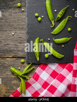 Offene und geschlossene Pellets von grünen Erbsen auf einem schwarzen Stein Hintergrund. Frisches Obst. Die Ernte. Ansicht von oben. Stockfoto