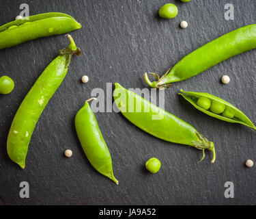 Offene und geschlossene Pellets von grünen Erbsen auf einem schwarzen Stein Hintergrund. Frisches Obst. Die Ernte. Ansicht von oben. Stockfoto