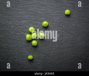 Erbsen, grüne Erbsen auf einem schwarzen Stein Hintergrund. Frisches Obst. Die Ernte. Ansicht von oben. Stockfoto