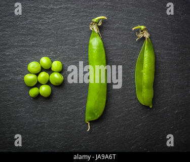 Offene und geschlossene Pellets von grünen Erbsen auf einem schwarzen Stein Hintergrund. Frisches Obst. Die Ernte. Ansicht von oben. Stockfoto