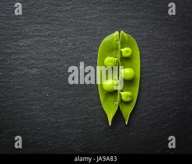 Offene und geschlossene Pellets von grünen Erbsen auf einem schwarzen Stein Hintergrund. Frisches Obst. Die Ernte. Ansicht von oben. Stockfoto