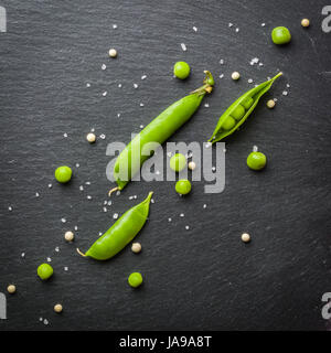 Offene und geschlossene Pellets von grünen Erbsen auf einem schwarzen Stein Hintergrund. Frisches Obst. Die Ernte. Ansicht von oben. Stockfoto