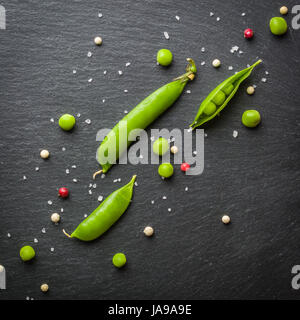 Offene und geschlossene Pellets von grünen Erbsen auf einem schwarzen Stein Hintergrund. Frisches Obst. Die Ernte. Ansicht von oben. Stockfoto