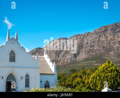 Malerische weisse Holländischen Kap Kirche, Franschhoek, Westkap, Südafrika, mit Bergkulisse und blauer Himmel Stockfoto