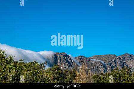 Wolken über die Berge wie ein Wasserfall, mit Weinberg im Vordergrund, Franschhoek, Westkap, Südafrika Stockfoto