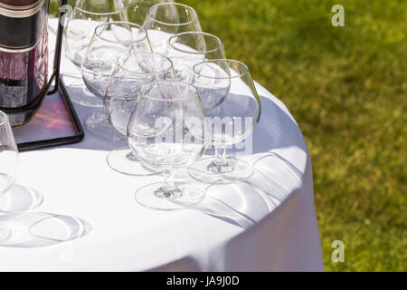 Transparente Gläser für Cognac mit großen Flasche auf weißen runden Tisch im Freien. Stockfoto