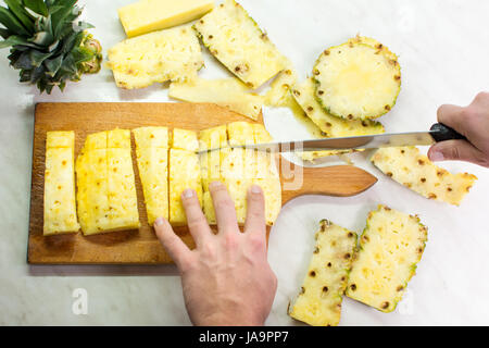 Männliche Hände schneiden Ananas Frucht auf einem Holzbrett Stockfoto