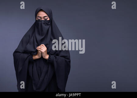 Junge asiatische muslimische Frau trägt Niqab beten mit dunklem Hintergrund Stockfoto
