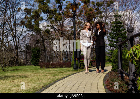Zwei schöne Geschäftsfrauen in Anzügen im Park spazieren und reden. Stockfoto