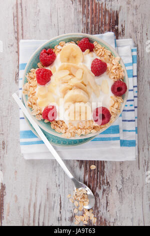 Haferflocken mit frischem Joghurt mit Himbeeren und Bananen mit Musli auf Holztisch von oben. Stockfoto