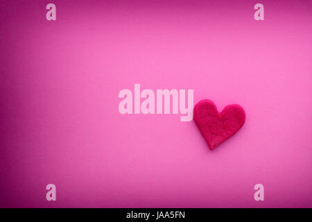 Rotes Herz mit kleinen Rissen auf einem rosa Hintergrund mit Vignette. Hautnah. Stockfoto