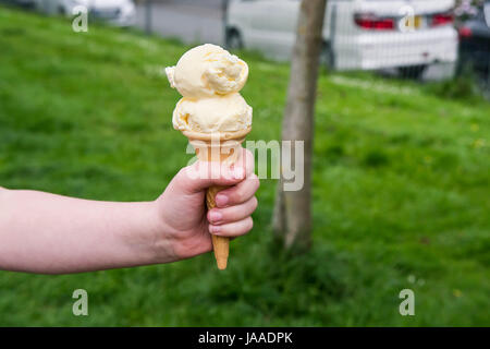 Ein Kind hält eine Eiswaffel; Hand; Kind; Zu behandeln; Vanille-Eis; Eiscreme-Kegel; Kornett; Doppelte Schaufel; Aktualisieren; Erfrischung; Stockfoto