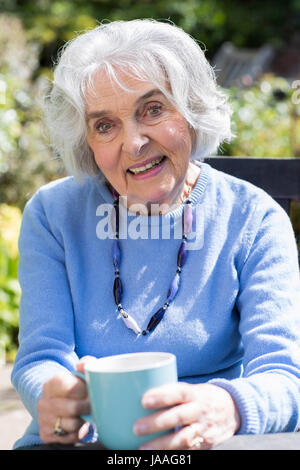 Portrait Of Senior Woman entspannend im Garten mit Heißgetränk Stockfoto