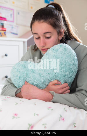 Junges Mädchen auf Bett umarmt Herz geformten Kissen liegend Stockfoto