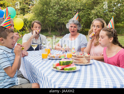 Familie kleine Mädchen Geburtstag außerhalb an Picknick-Tisch weht Partei Hörner Stockfoto