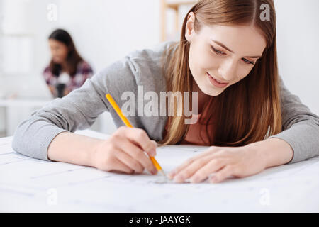 Die Gedanken real. Anhaltende talentierte hübsche Dame macht einen Entwurf, Zeichnung auf das neue Gebäude bei der Nutzung einige spezielle Werkzeuge dafür precisene Stockfoto