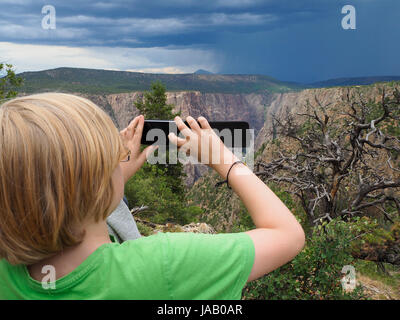Ein Junge nimmt ein Bild von einem herannahenden Gewitter mit seinem Smartphone im "Black Canyon des Gunnison" National Park (Colorado, USA). Stockfoto