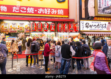 Dotonbori, Osaka. Die Menschen Schlange, um traditionelle japanische Küche, Takoyaki und Okonomiyaki von Take-away zu kaufen Zähler im Laufe des Abends. Stockfoto