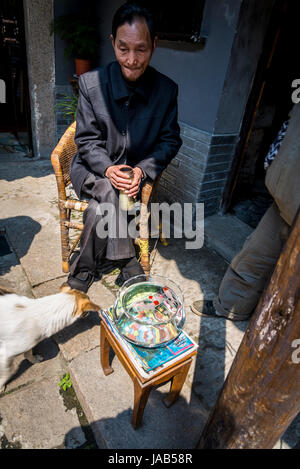 Chinesischer Mann sitzt vor seinem Haus mit Goldfischglas vor ihm, antiken Stadt Tongli, Suzhou, Provinz Jiangsu, China Stockfoto