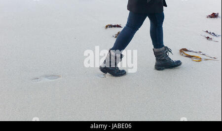 Füße und Beine der jungen Frau in nassen Sand am Meeresstrand und hinterlassen Spuren. Sennen Cove, Cornwall, Großbritannien Stockfoto