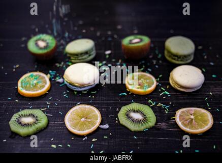 Grüne und weiße Makronen mit Kiwi, Orange und Zitrone in Reihenfolge auf einem Tisch Holz gark Stockfoto