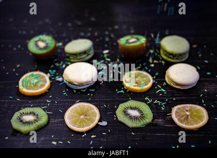 Grüne und weiße Makronen mit Kiwi, Orange und Zitrone in Reihenfolge auf einem Tisch Holz gark Stockfoto