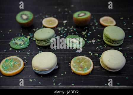 Grüne und weiße Makronen mit Kiwi, Orange und Zitrone in Reihenfolge auf einem Tisch Holz gark Stockfoto