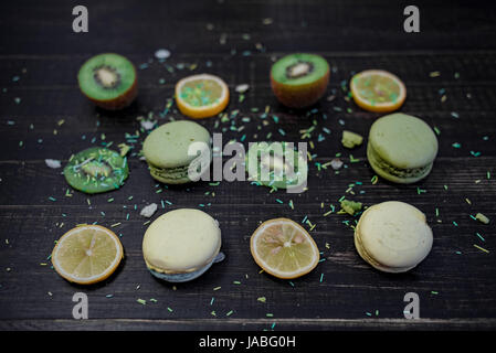 Grüne und weiße Makronen mit Kiwi, Orange und Zitrone in Reihenfolge auf einem Tisch Holz gark Stockfoto